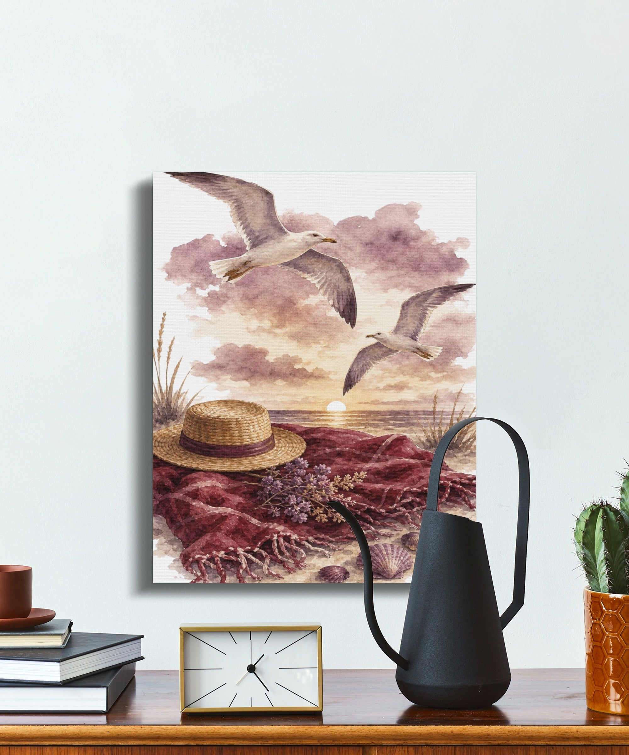 Watercolor painting of two seagulls flying over a beach scene with a straw hat and blanket.