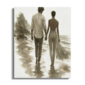 Couple holding hands walking on a wet sandy beach with a rocky cliff background.